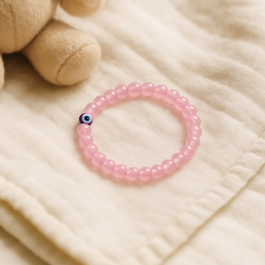 Rose Quartz Children’s Nazar Suraksha, Evil Eye Protection Bracelet with a blue and green bead on a beige fabric background