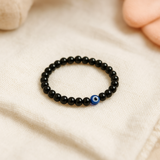 Obsidian Children’s Nazar Suraksha bracelet with a blue evil eye charm on a beige fabric background. Buri nazar bracelet for kids.