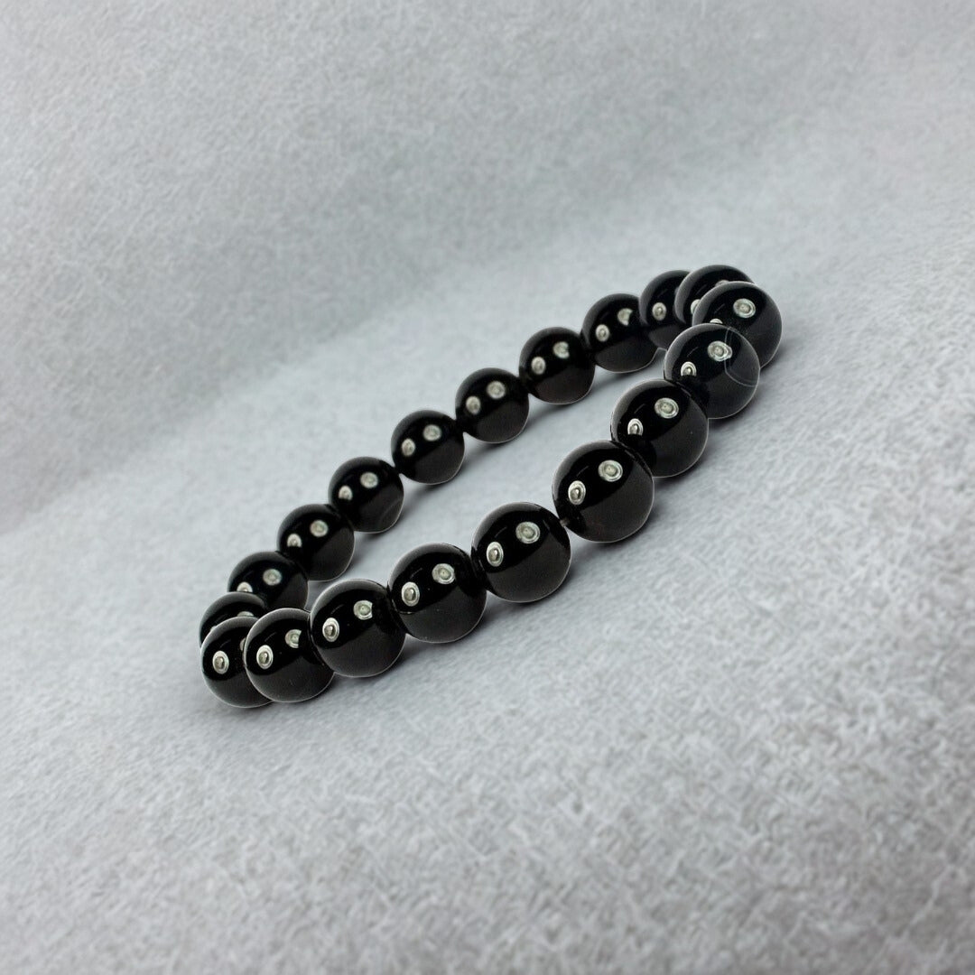 Black beaded bracelet with silver beads on a light gray background