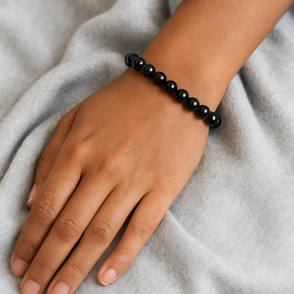 Black beaded bracelet on a wrist against a gray fabric background
