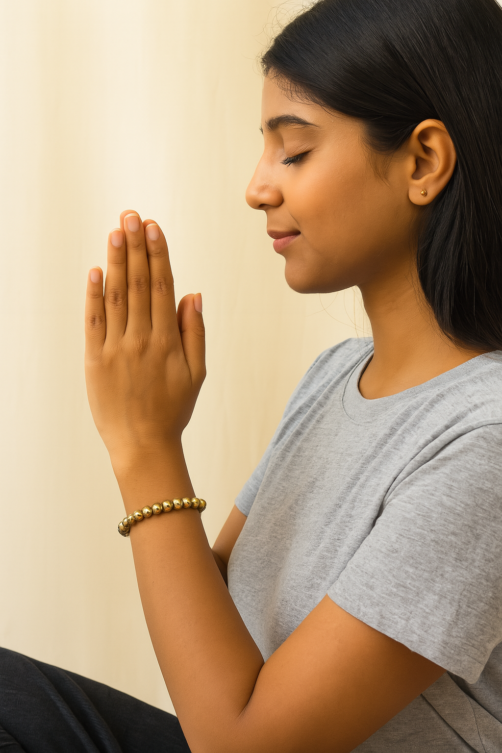 Woman in a gray shirt with hands pressed together in a gesture of prayer against a plain background