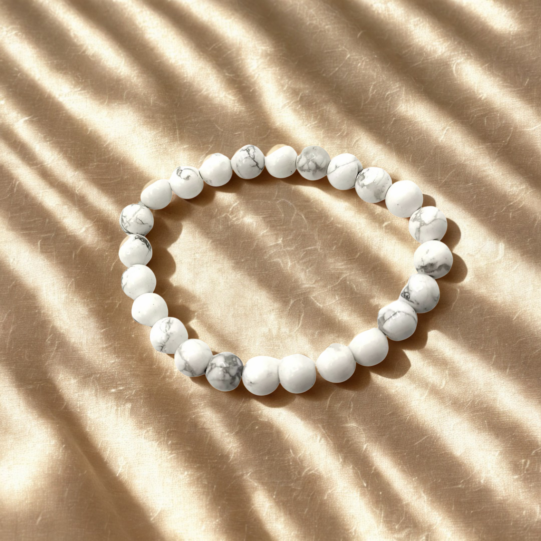 White beaded bracelet on a beige surface with shadow patterns