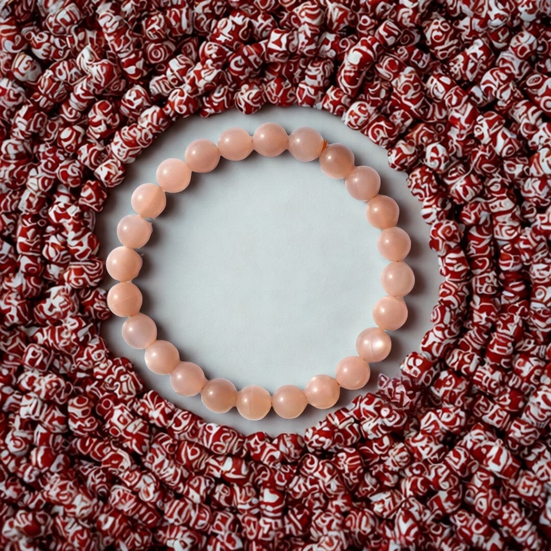 Pink beaded bracelet on a white background with red patterned beads surrounding it