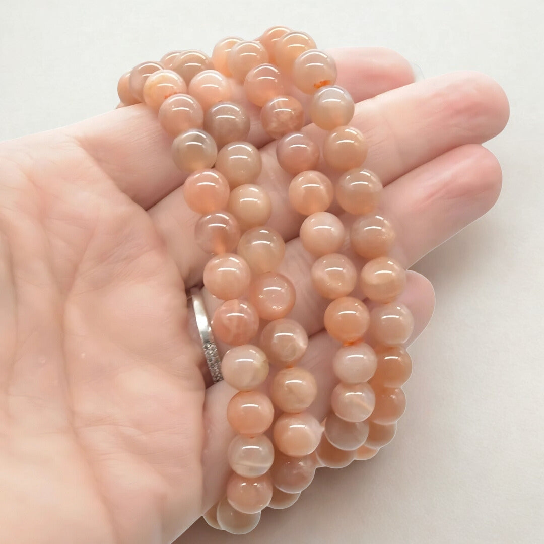 Hand holding a stack of peach-colored beads against a white background
