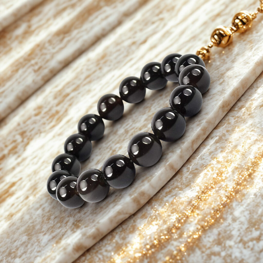 Black beaded bracelet with a gold clasp on a light wood surface