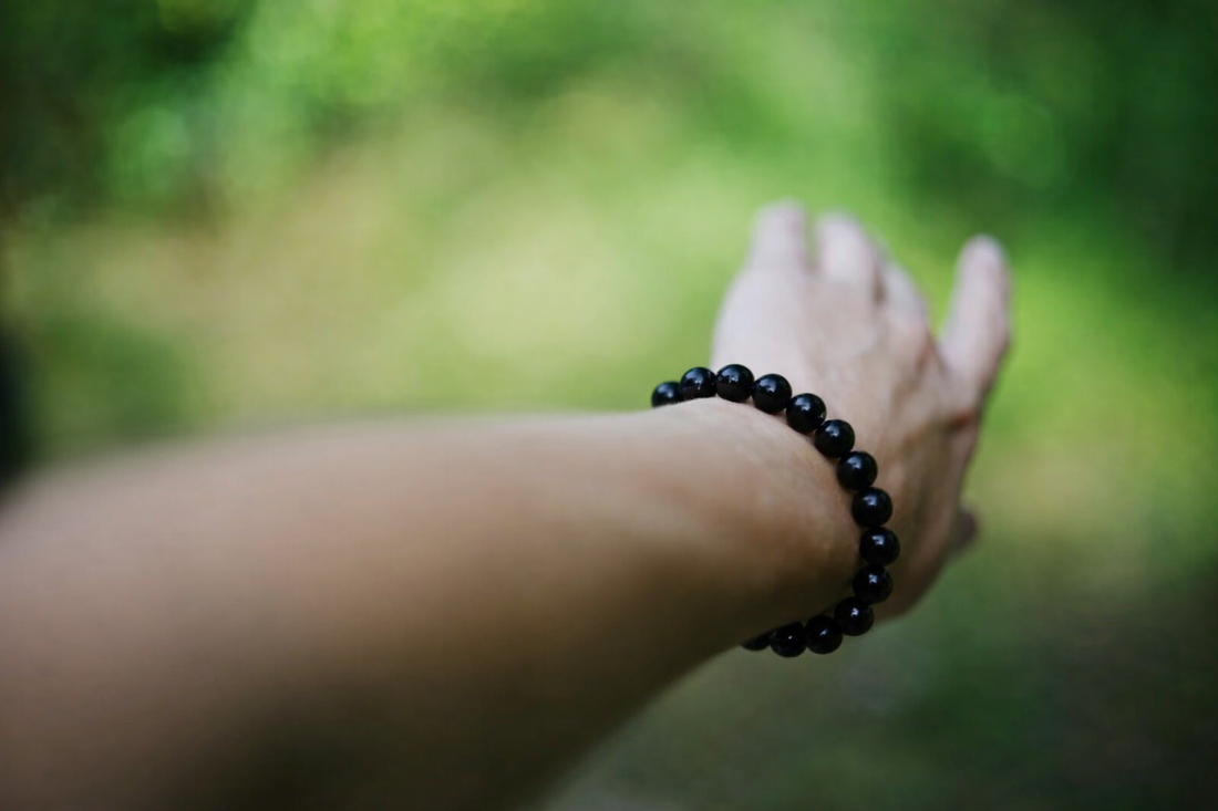 Black obsidian bracelet worn on hand against a natural green background symbolizing protection and grounding energy