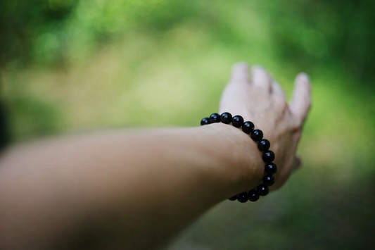 Black obsidian bracelet worn on hand against a natural green background symbolizing protection and grounding energy