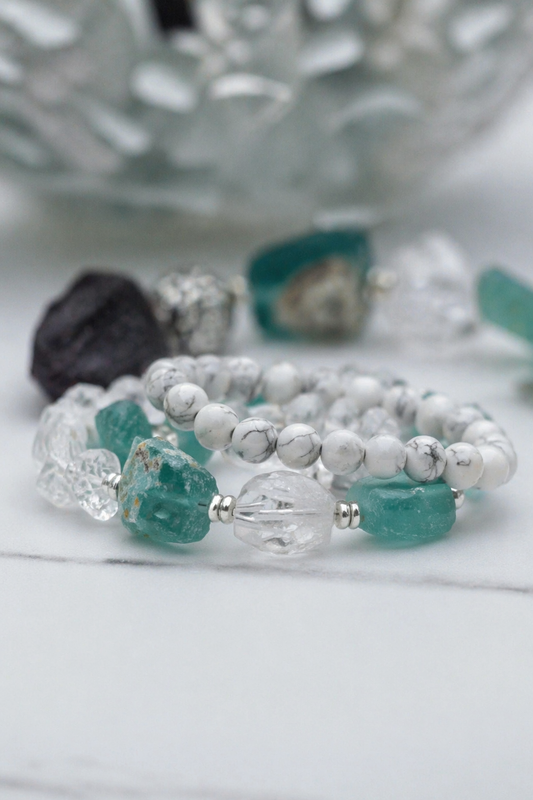 White howlite bead bracelets stacked with crystal bracelets including clear quartz and green stones in a soft natural setting for calming and healing energy use