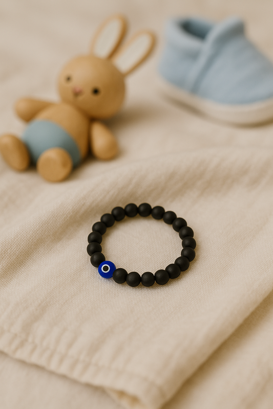 Karungali Children’s Nazar Suraksha bracelet with a blue bead on a beige surface, next to a plush bunny and baby booties.