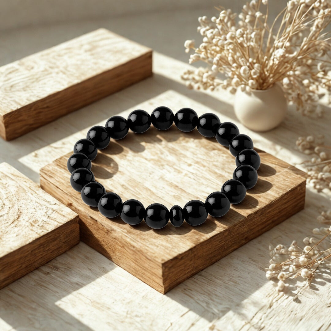 Black beaded bracelet on a wooden surface with dried flowers in the background