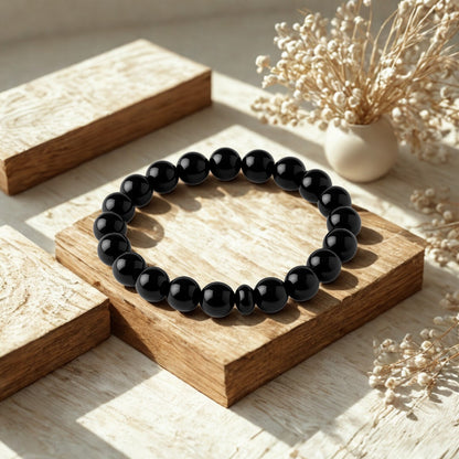 Black beaded bracelet on a wooden surface with dried flowers in the background