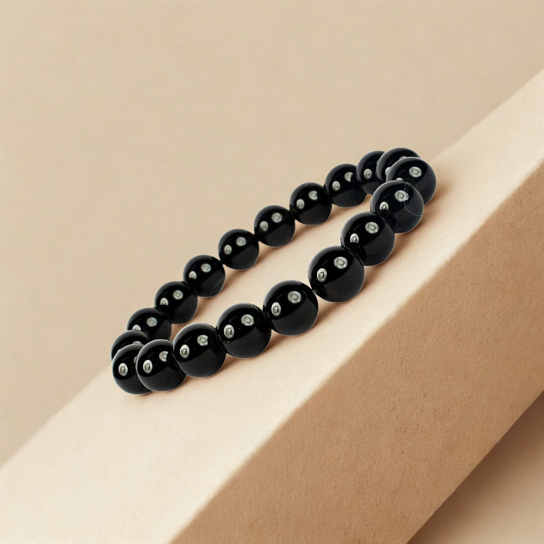 Black beaded bracelet with silver beads on a beige surface