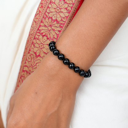Black beaded bracelet on a wrist with a white and red patterned fabric background