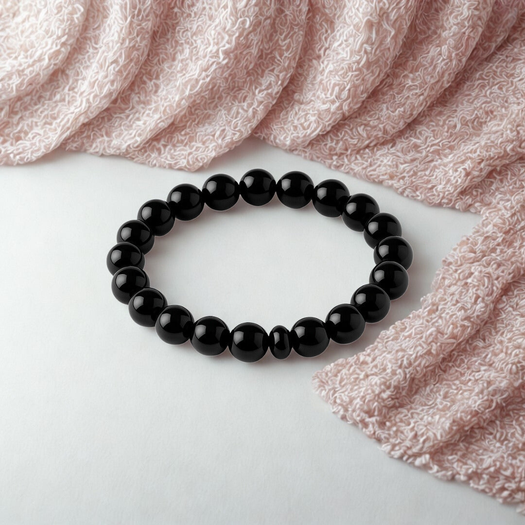 Black beaded bracelet on a white surface with pink fabric in the background