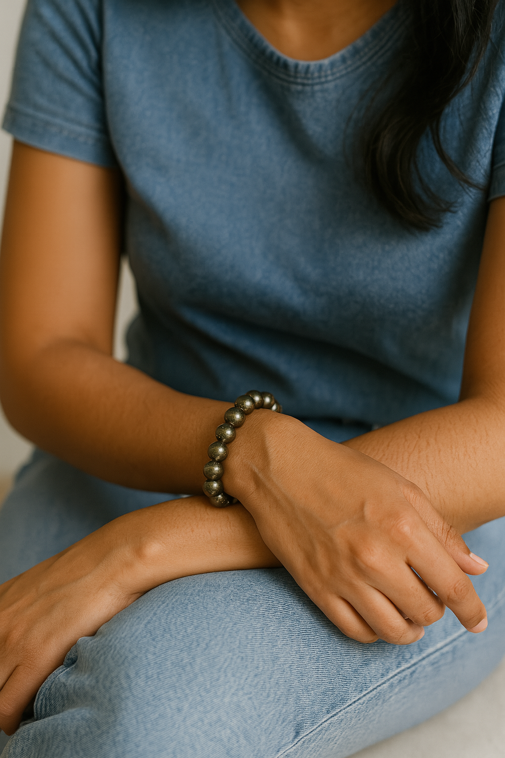Person wearing a blue shirt and light blue jeans with a bracelet on a neutral background