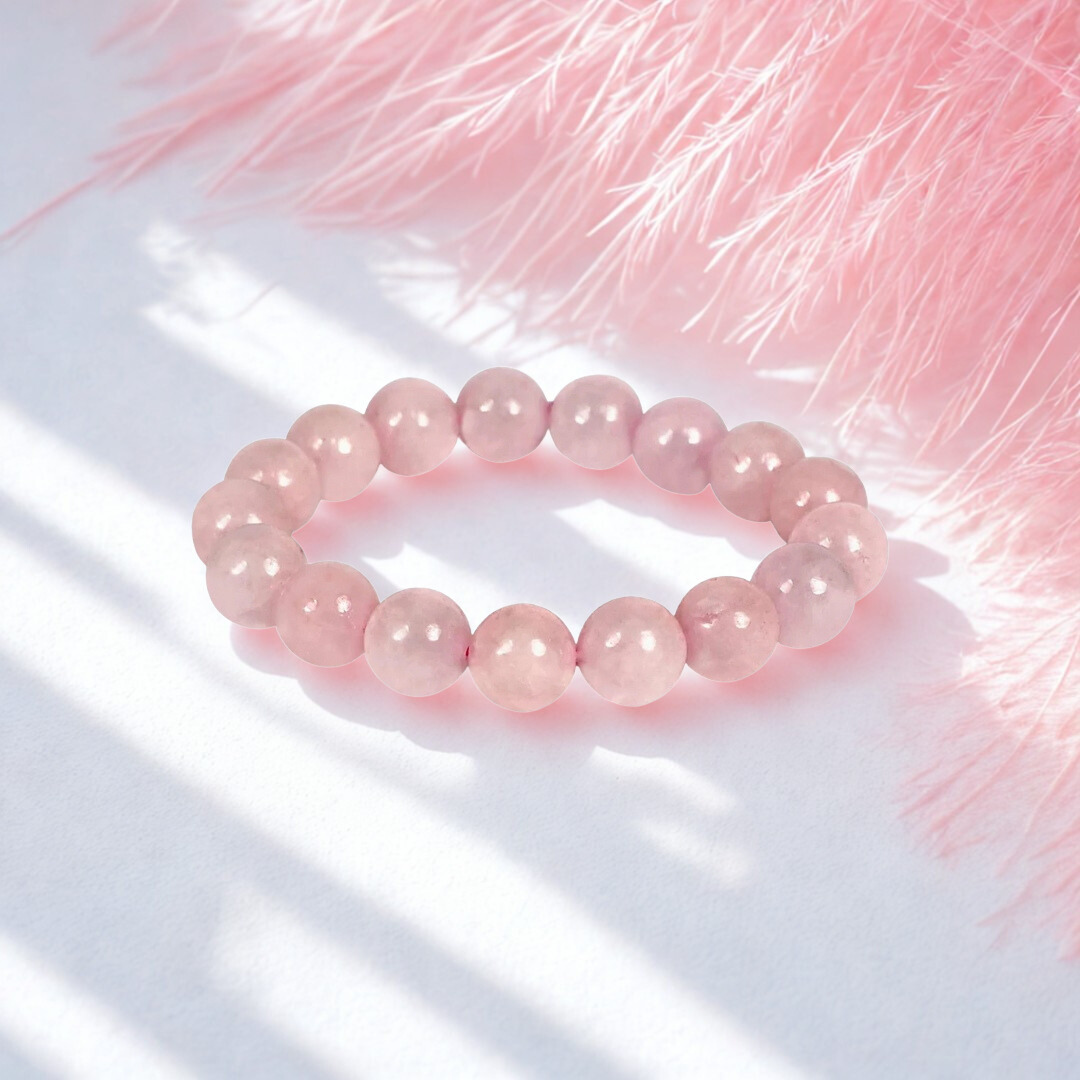 Pink beaded bracelet on a white surface with pink feathers in the background