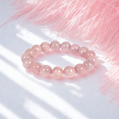 Pink beaded bracelet on a white surface with pink feathers in the background