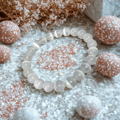 White beaded bracelet on a textured surface with decorative stones and dried flowers.