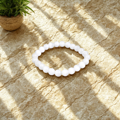 White beaded bracelet on a textured stone surface with a plant in the corner