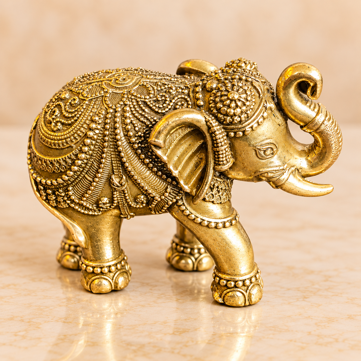 Close angled view of brass elephant showing its carved ornamental covering, raised trunk and headpiece