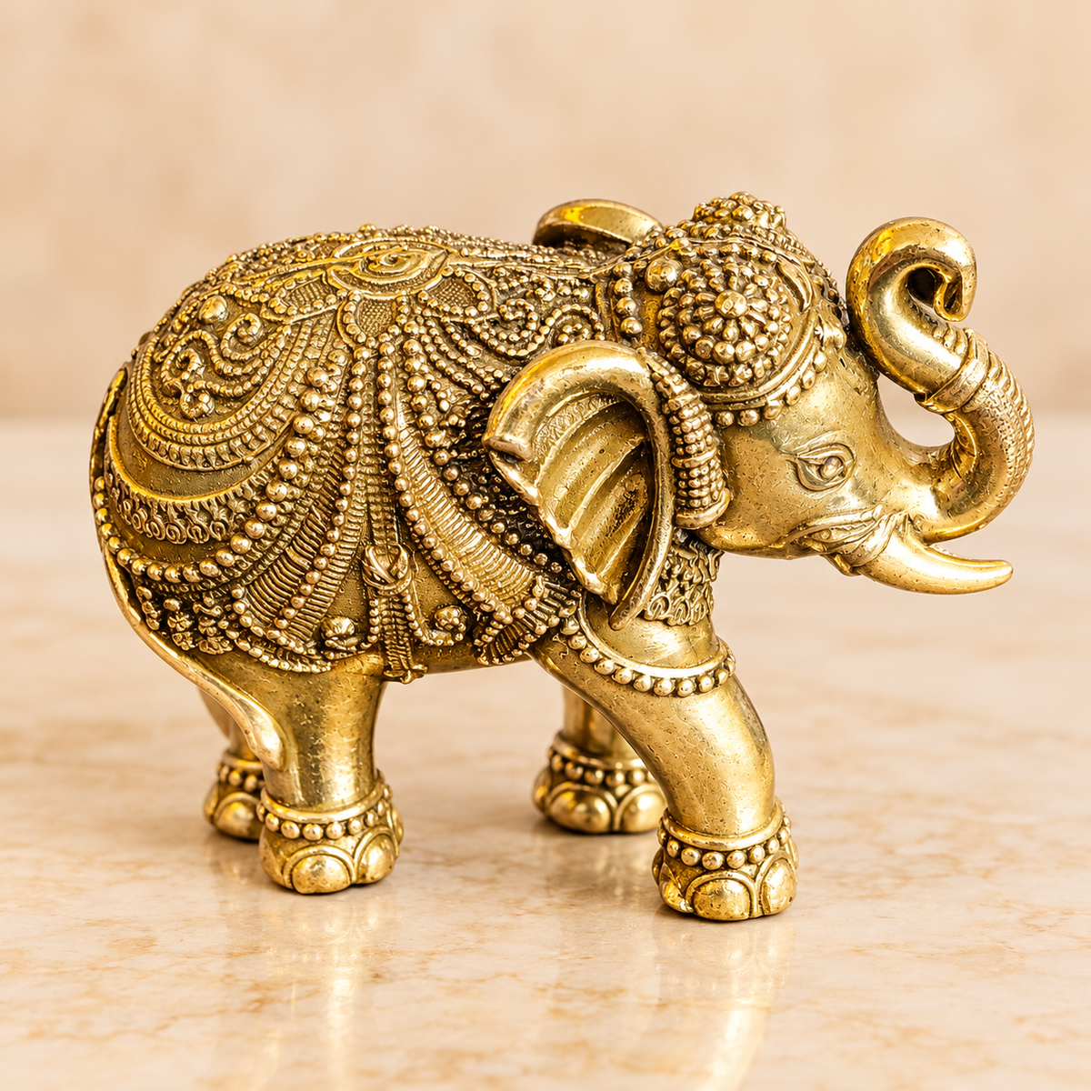 Ornate golden brass elephant figurine with upward-curved trunk, decorative saddle, tusks and detailed feet
