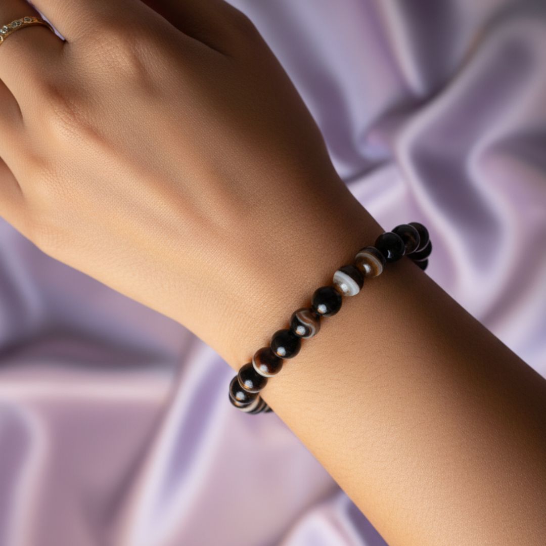 Hand wearing a black sulemani hakik bracelet against a soft purple fabric background